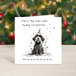 May include: A Christmas card with a black and white dog wearing a party hat. The card reads "Deck the halls with muddy footprints..." and "Fa la la la la, la la la la..." against a blurred Christmas tree background.