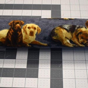 May include: A rolled-up fabric featuring a repeating pattern of various dog breeds in shades of brown, tan, and black against a dark blue background. The dogs are depicted in various poses, creating a playful and charming design.