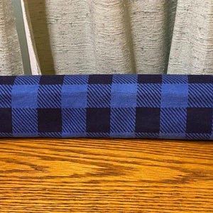 May include: A blue and black buffalo plaid fabric door draft stopper. The rectangular stopper is made of fabric and is designed to block drafts from entering under a door. The plaid pattern is a classic design.
