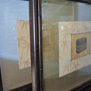 May include: Two framed art pieces with bamboo-style dark brown frames. Each piece features a light beige background with a bamboo leaf pattern. A central square contains a drawing of a stacked box in shades of brown and gold.