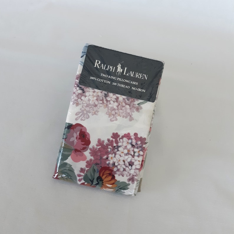 Op de afbeelding: Twee kingsize kussenslopen in een bloemenprint met roze, witte en rode bloemen op een witte achtergrond. De verpakking bevat het Ralph Lauren logo en de tekst "Two King Pillowcases 100% Cotton 200 Thread No-Iron."