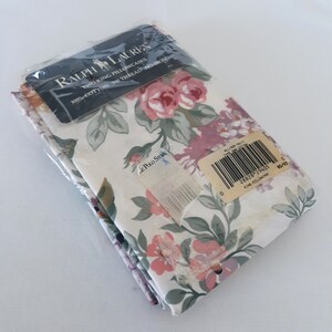 Op de afbeelding: Twee witte kingsize kussenslopen met een bloemenpatroon met roze, paarse en groene bloemen. De kussenslopen zijn verpakt in plastic en hebben een Ralph Lauren Polo Store-label.