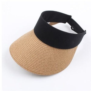 May include: A brown straw visor with a black fabric band around the crown. The visor is made of woven straw and has a wide brim.