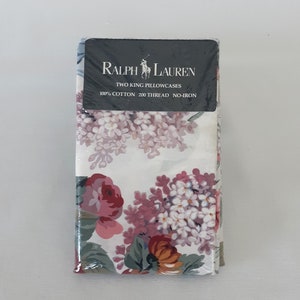 Op de afbeelding: Twee kingsize kussenslopen in een witte bloemenprint met roze, paarse en oranje bloemen. De verpakking bevat het Ralph Lauren logo en de tekst "Two King Pillowcases 100% Cotton 200 Thread No-Iron."
