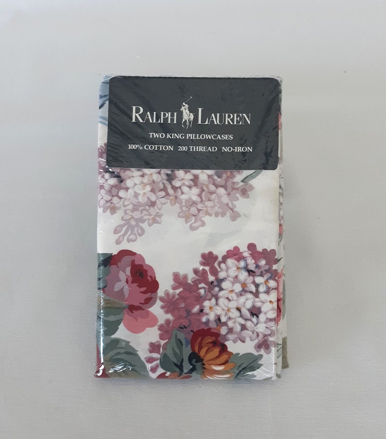 Op de afbeelding: Twee kingsize kussenslopen in een witte bloemenprint met roze, paarse en oranje bloemen. De verpakking bevat het Ralph Lauren logo en de tekst "Two King Pillowcases 100% Cotton 200 Thread No-Iron."