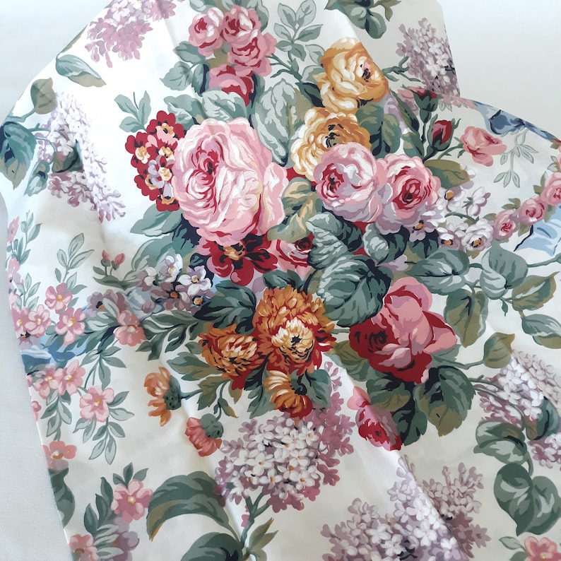 Op de afbeelding: Een witte stof met een bloemenpatroon met roze, rode, gele en groene bloemen. De stof heeft een vintage uitstraling en is perfect voor knutselprojecten.