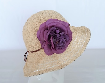 May include: A beige crochet sun hat with a large purple flower accent.