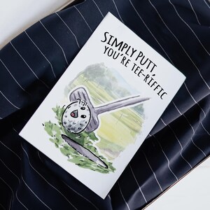 May include: A white card with a watercolor illustration of a golf ball and club. The text on the card reads "Simply Putt, You're Tee-Rific".