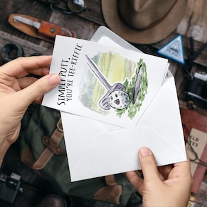 May include: A white card with a watercolor illustration of a golf club and golf ball. The text on the card reads "Simply Putt, You're Tee-Rific".
