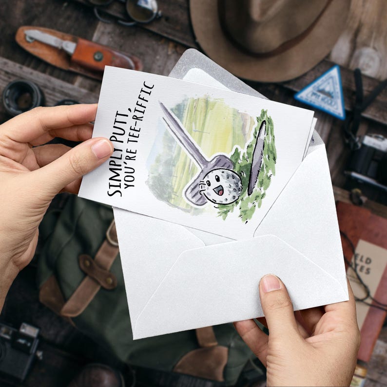 May include: A white card with a watercolor illustration of a golf club and golf ball. The text on the card reads "Simply Putt, You're Tee-Rific".