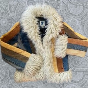 Puede incluir: Una chaqueta vaquera vintage con cuello y ribete de piel sintética color crema. Las mangas y los paneles frontales presentan un diseño de patchwork con tonos de azul, marrón y dorado. La chaqueta tiene una estética retro clásica.