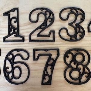 May include: Set of ten black metal house numbers with a decorative, ornate design. The numbers are 0 through 9.