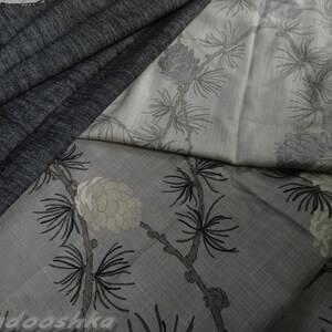 May include: Close-up of folded fabric in shades of grey and off-white. The fabric features a botanical print of pine cones and branches. The top left corner shows a darker grey, textured fabric. The overall design is elegant and natural.