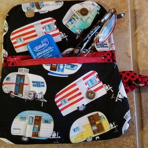 May include: A black fabric zippered pouch with a red zipper and a red and black polka dot strap. The pouch is decorated with a pattern of vintage camper trailers. The pouch is open and contains a blue Glide Pro-Health mouthwash and a pair of glasses.