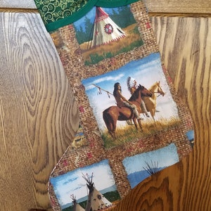 May include: A green and brown Christmas stocking with a Native American theme. The stocking features images of teepees, horses, and Native American figures. The top of the stocking is green with a swirling pattern.