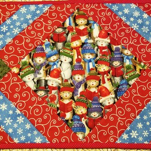 Könnte beinhalten: Ein roter, blauer und grüner gesteppter Tischläufer mit einem Rautenmuster. Die mittlere Raute zeigt einen festlichen Druck von Katzen, die Wintermützen und Schals tragen.