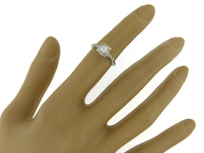 May include: A silver ring with a round, clear center stone and smaller stones on the band.