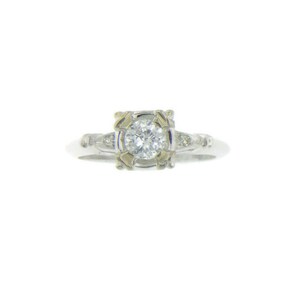 May include: A silver ring with a round, clear diamond set in a square frame. The frame has a gold-toned design. The ring has smaller diamonds on the band.