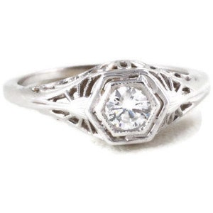 May include: A silver filigree engagement ring with a round, clear diamond in the center.