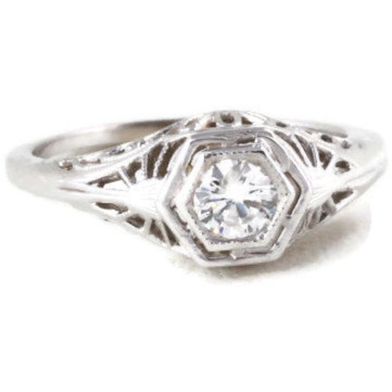 May include: A silver filigree engagement ring with a round, clear diamond in the center.