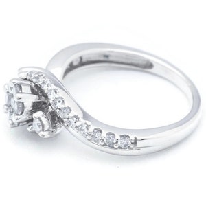 Op de afbeelding: Een zilveren ring met een cluster van kleine diamanten die in een swirl-ontwerp zijn gezet. De ring ligt op een witte achtergrond.