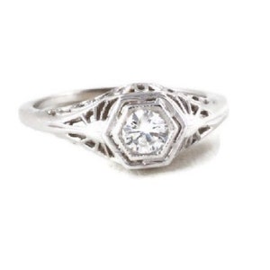 May include: A silver ring with a delicate filigree design and a single round diamond in the center.