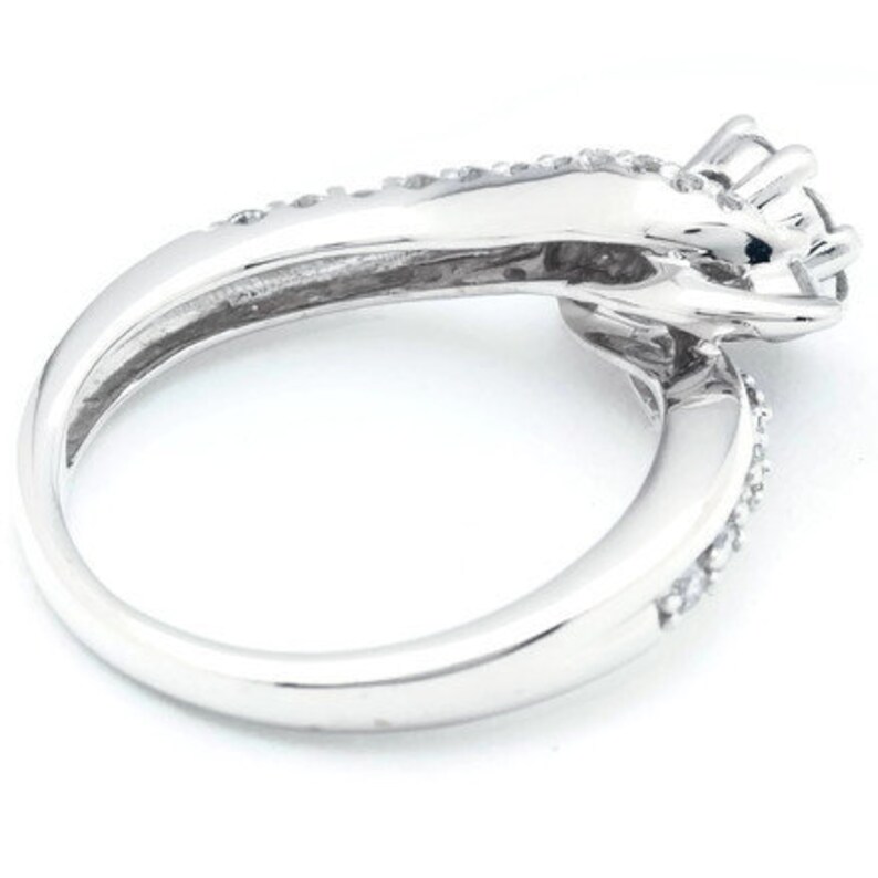 Op de afbeelding: Een zilveren ring met een grote, heldere edelsteen omringd door kleinere edelstenen. De ring is ontworpen om eruit te zien als twee handen die de edelsteen vasthouden.