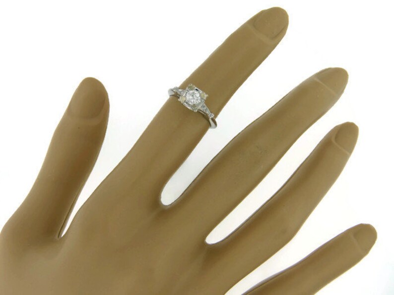 May include: A silver ring with a round, clear center stone and smaller stones on the band.