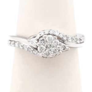 Op de afbeelding: Een zilveren ring met een cluster van diamanten in een swirl-ontwerp.