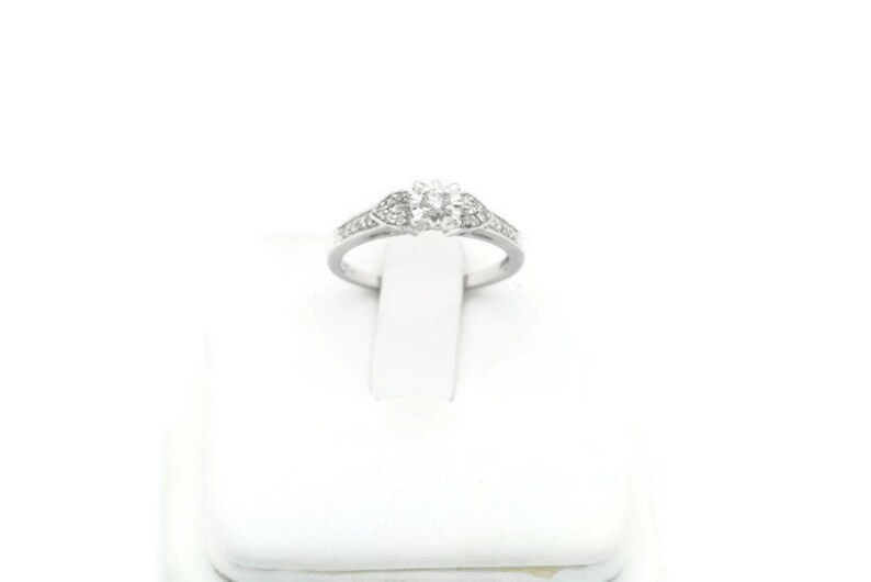 May include: A silver ring with a single round diamond in the center and smaller diamonds set in the band.