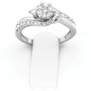 Op de afbeelding: Een zilveren ring met een cluster van kleine diamanten in het midden en kleinere diamanten die langs de band zijn gezet.