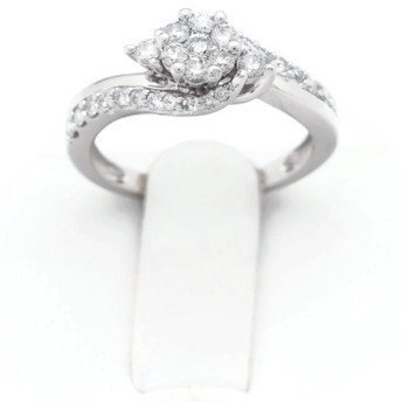 Op de afbeelding: Een zilveren ring met een cluster van kleine diamanten in het midden en kleinere diamanten die langs de band zijn gezet.