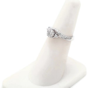 Op de afbeelding: Een zilveren ring met een cluster van kleine diamanten gezet in een swirl-ontwerp. De ring is op een witte ringstandaard.