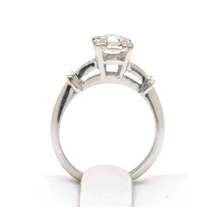 May include: A silver engagement ring with a single round diamond in the center and two smaller diamonds on the band.