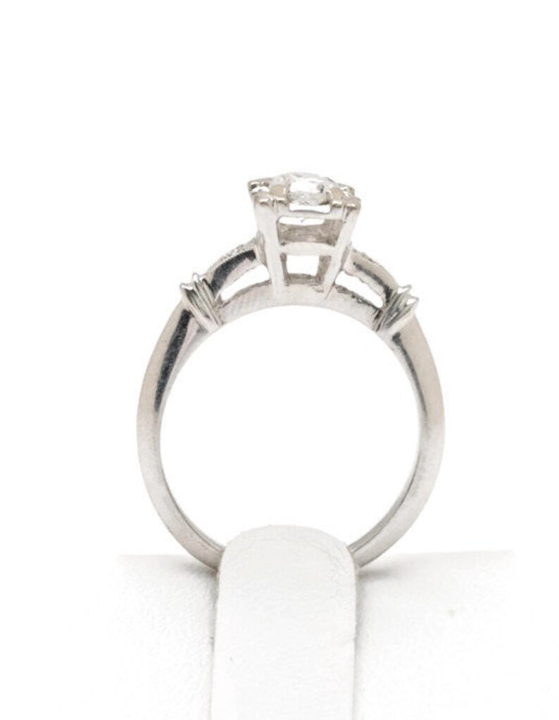 May include: A silver engagement ring with a single round diamond in the center and two smaller diamonds on the band.
