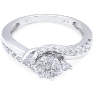 Op de afbeelding: Een zilveren ring met een cluster van diamanten in het midden en een rij diamanten rond de band. De ring is gemarkeerd met "IKS" aan de binnenkant.
