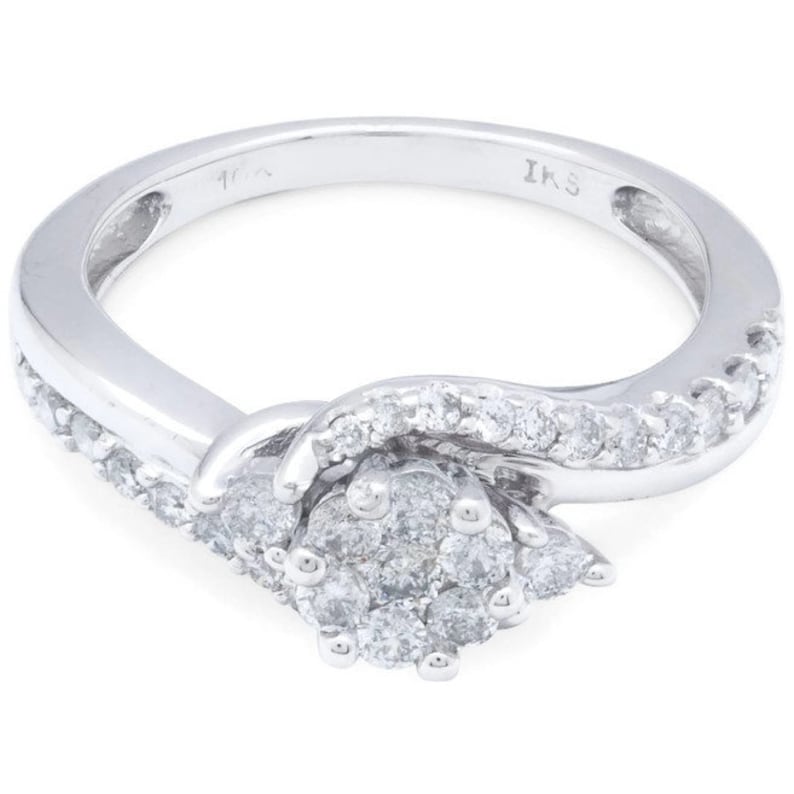Op de afbeelding: Een zilveren ring met een cluster van diamanten in het midden en een rij diamanten rond de band. De ring is gemarkeerd met "IKS" aan de binnenkant.