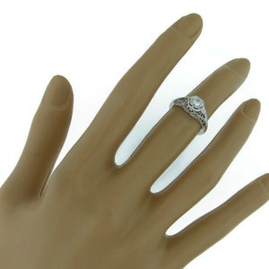 May include: A white gold engagement ring with a filigree design and a single round diamond in the center.
