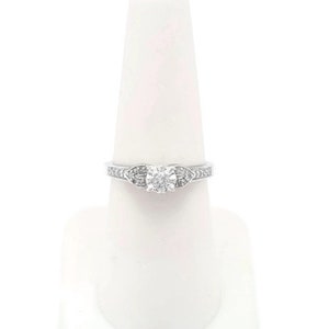 May include: A silver engagement ring with a round center diamond and smaller diamonds set in the band.