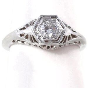 May include: A silver filigree engagement ring with a single round diamond set in a hexagonal bezel.