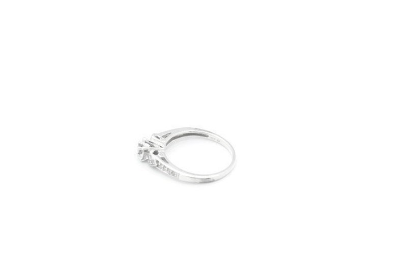 May include: A silver ring with a small cluster of diamonds in the center and smaller diamonds set along the band.