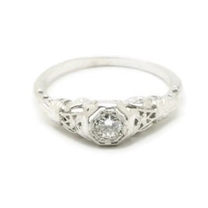May include: A silver ring with a delicate filigree design and a single round diamond in the center.