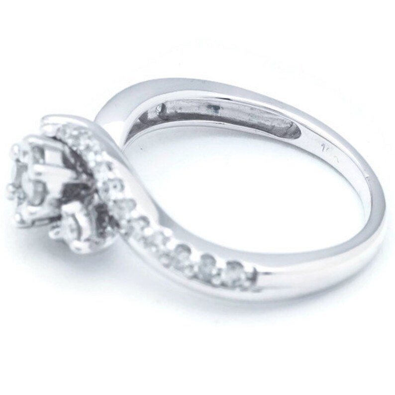 Op de afbeelding: Een zilveren ring met een cluster van kleine diamanten die in een swirl-ontwerp zijn gezet. De ring heeft een gepolijste afwerking en is geplaatst op een witte achtergrond.