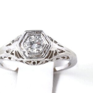 May include: A silver filigree ring with a single round diamond set in a hexagonal bezel.