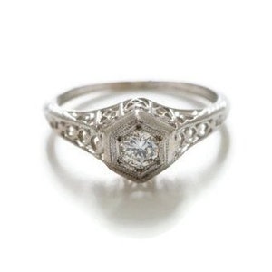 May include: A delicate silver ring with a filigree design and a single round diamond in the center.