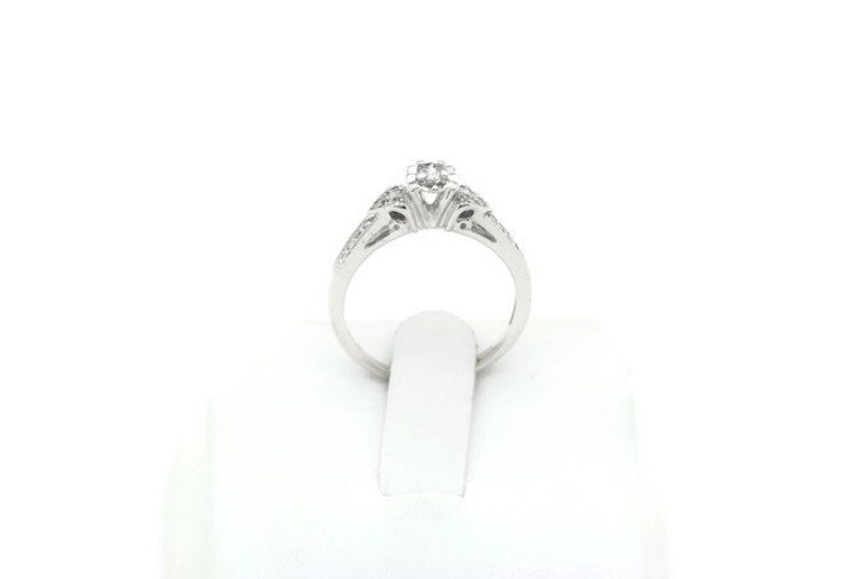 May include: A silver engagement ring with a single round diamond in the center and smaller diamonds set in the band.