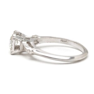 May include: A silver engagement ring with a single diamond set in a prong setting. The ring has a delicate, intricate design and is marked "14K" on the inside of the band.