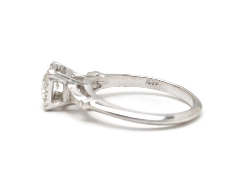 May include: A silver engagement ring with a single diamond set in a prong setting. The ring has a delicate, intricate design and is marked "14K" on the inside of the band.