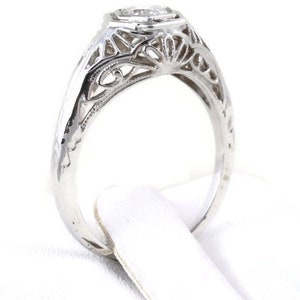 May include: A silver filigree engagement ring with a round, clear center stone.