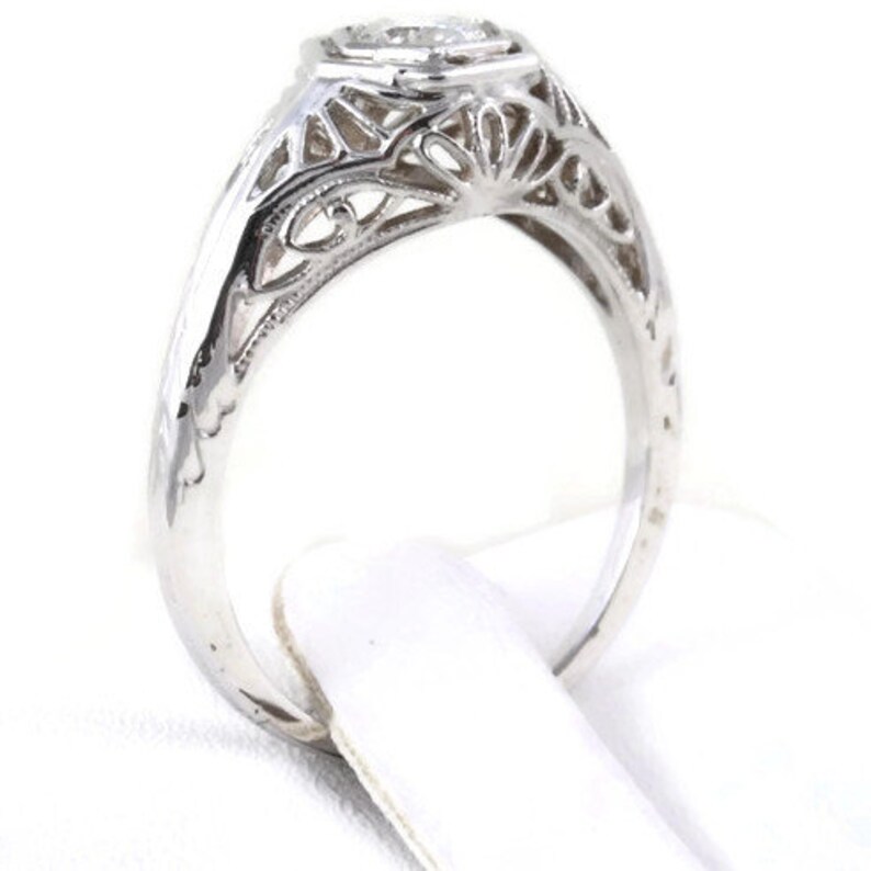 May include: A silver filigree engagement ring with a round, clear center stone.
